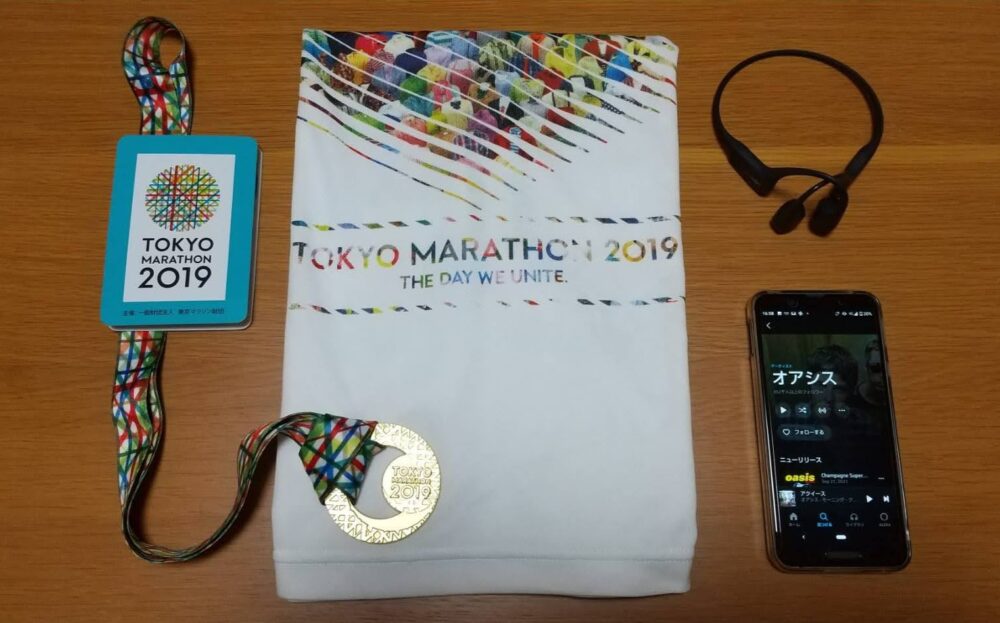 東京マラソン2019で貰ったTシャツと、完走メダル、コースマップ。ワイヤレスイヤホンと音楽再生中のスマートフォンの写真画像