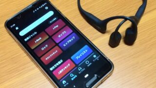 サブスクリプション型の音楽アプリを使用しているスマートフォンと、ワイヤレス骨伝導イヤホンの写真