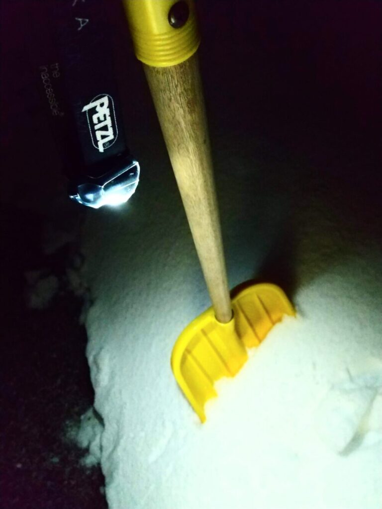 雪かきスコップにPETZL（ペツル）のヘッドライト「ティカ（黒）」をぶら下げた状態の写真
