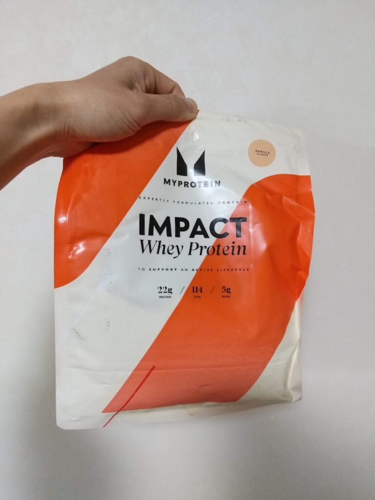 マイプロテインのImpactホエイプロテインバニラ味1kgの袋を手に持っている写真